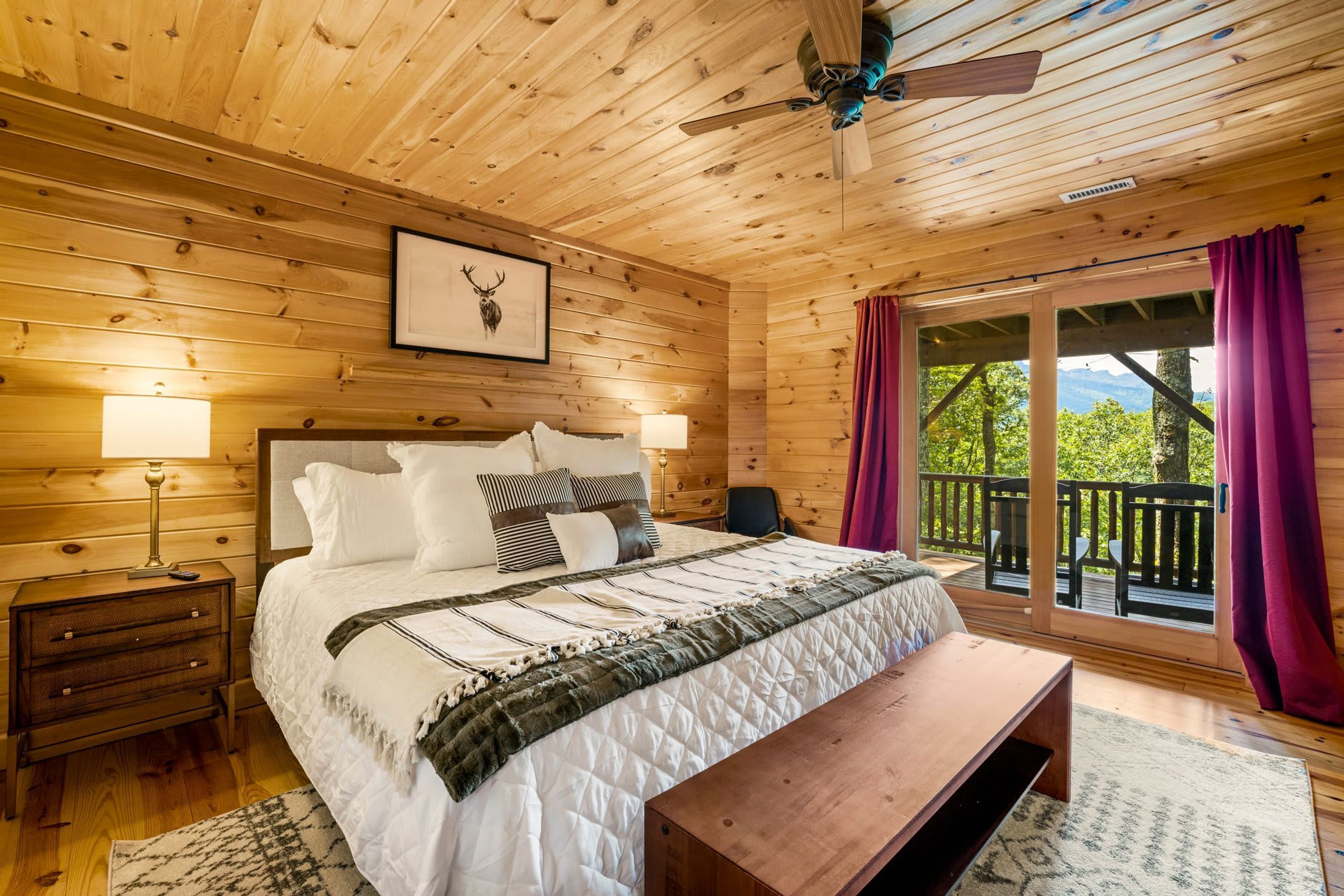 A wooden cabin bedroom with a bed, bedside lamps, a bench, and a balcony with curtains.