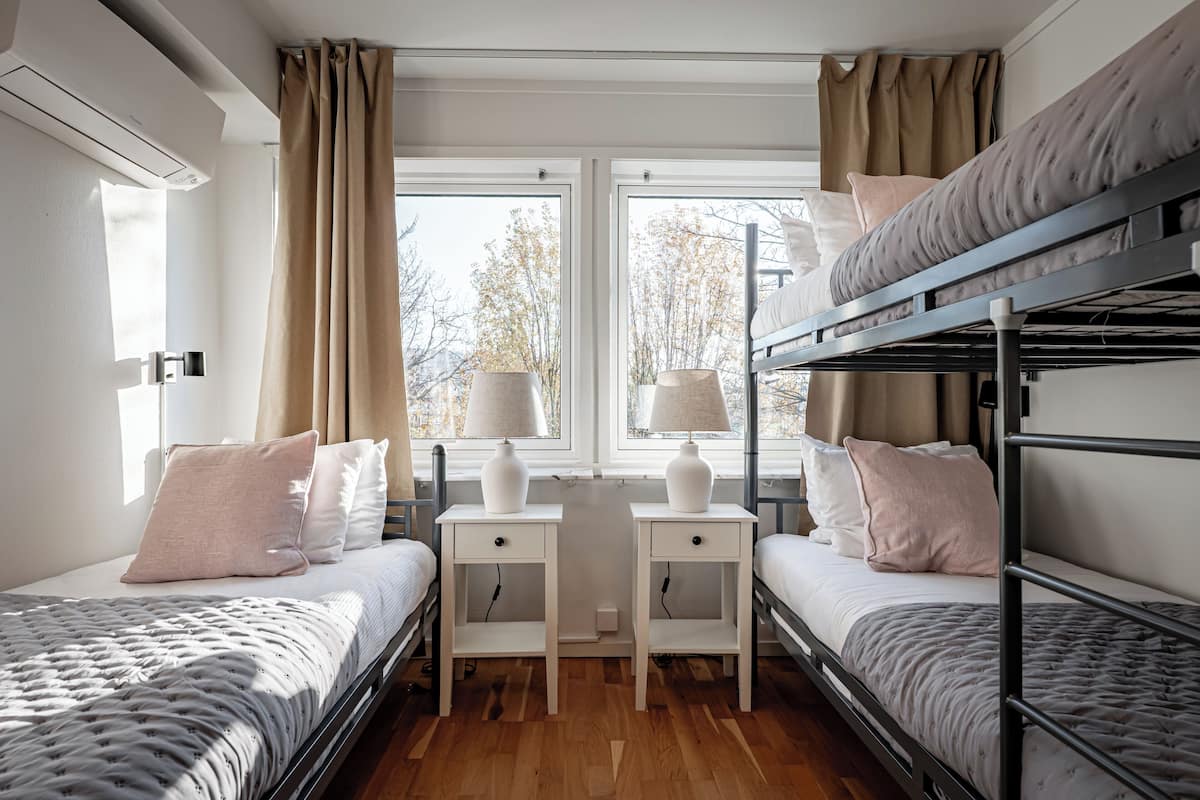 A bunk bed room with two bedside tables, a window with curtains, and an air conditioning unit.