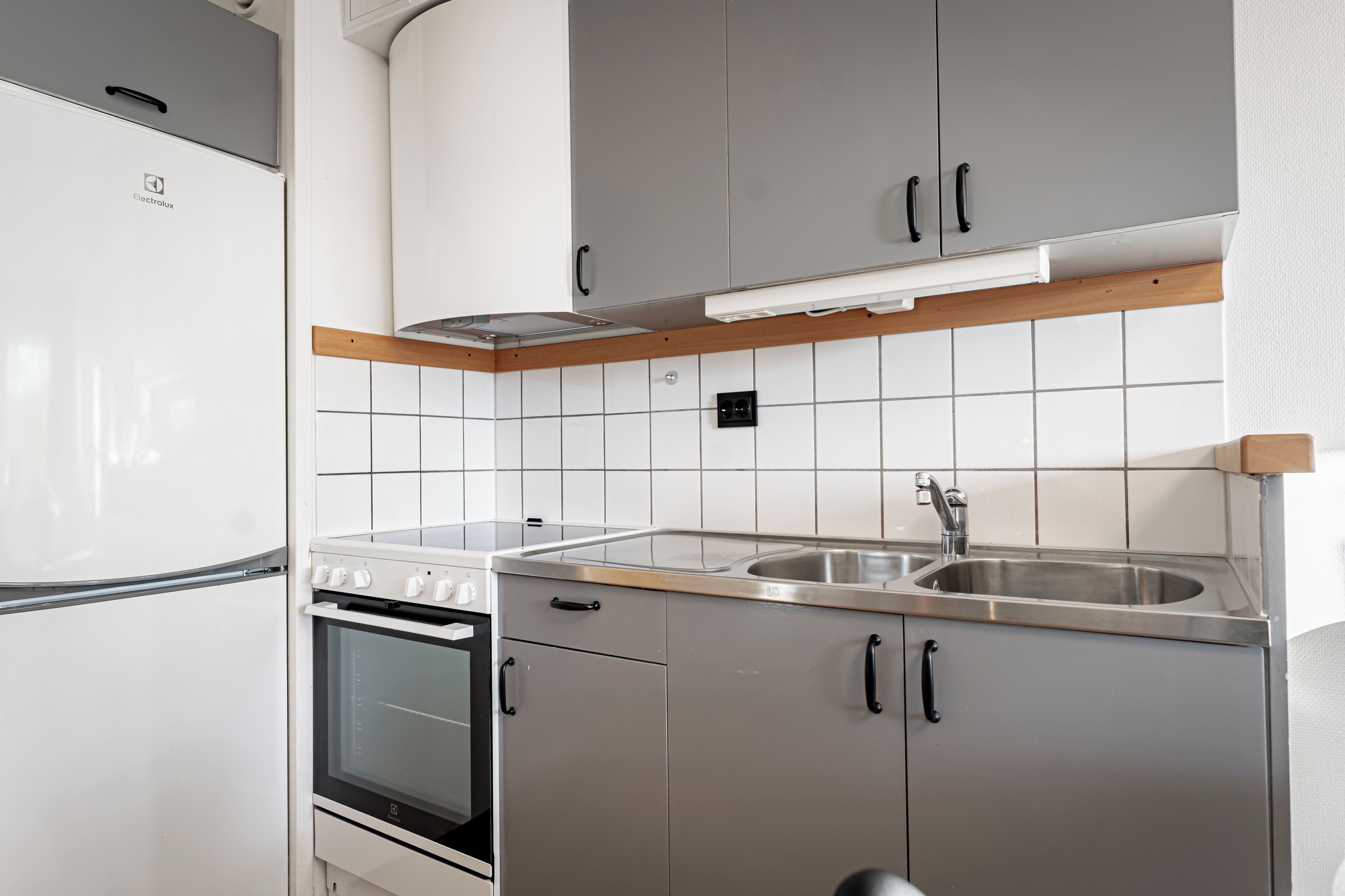 Una cocina moderna con refrigerador, horno, pileta de acero inoxidable y gabinetes grises.