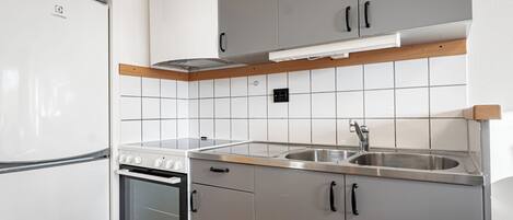 Una cocina moderna con refrigerador, horno, pileta de acero inoxidable y gabinetes grises.