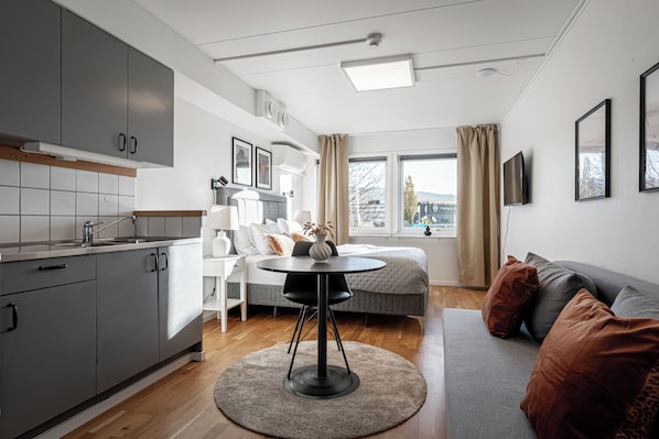 A modern kitchen with grey cabinets, a dining table with chairs, a sofa, and a TV. - Injoy Hotel Jönköping North (Jonkoping)