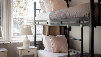 Una cama individual con almohadas, una mesita de noche con lámpara y una ventana con vista a árboles.