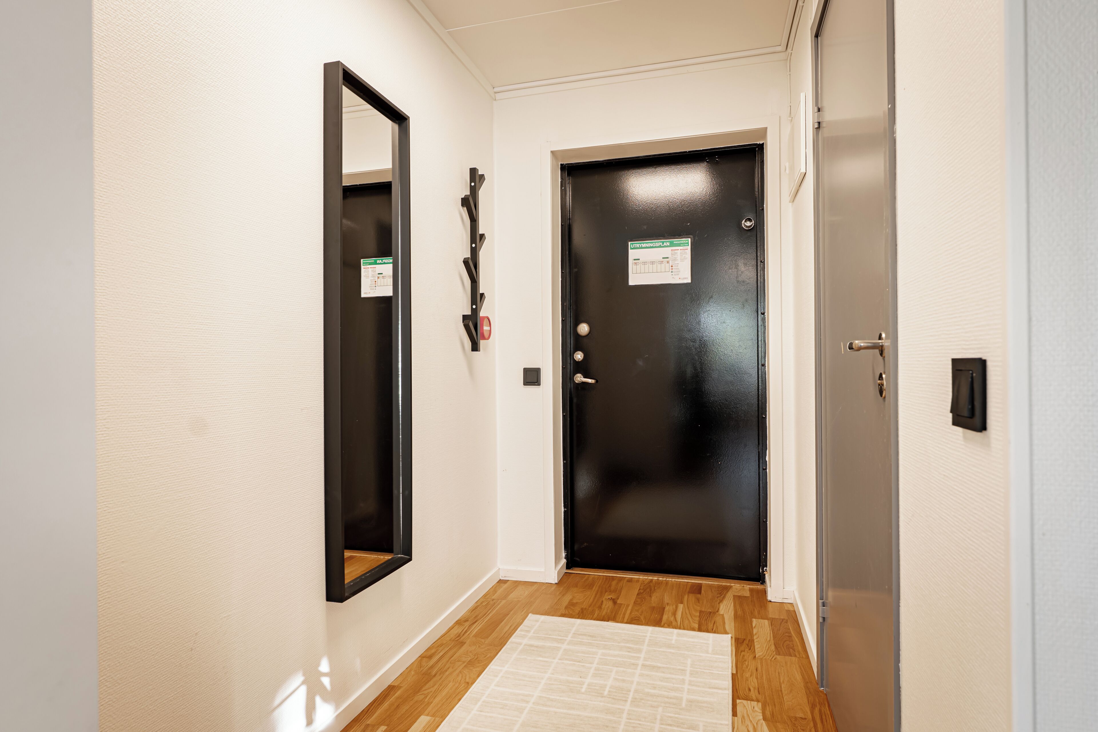 A hallway with a black door, a mirror, and a wooden floor.