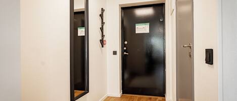 Un pasillo con una puerta negra, un espejo y piso de madera.