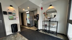 Passadís d'hotel amb un frigorífic, una màquina expenedora, un mirall i una estant amb objectes.
