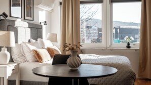 Una habitació d'hotel amb un llit, una taula rodona, un vas amb flors i una finestra amb cortines.