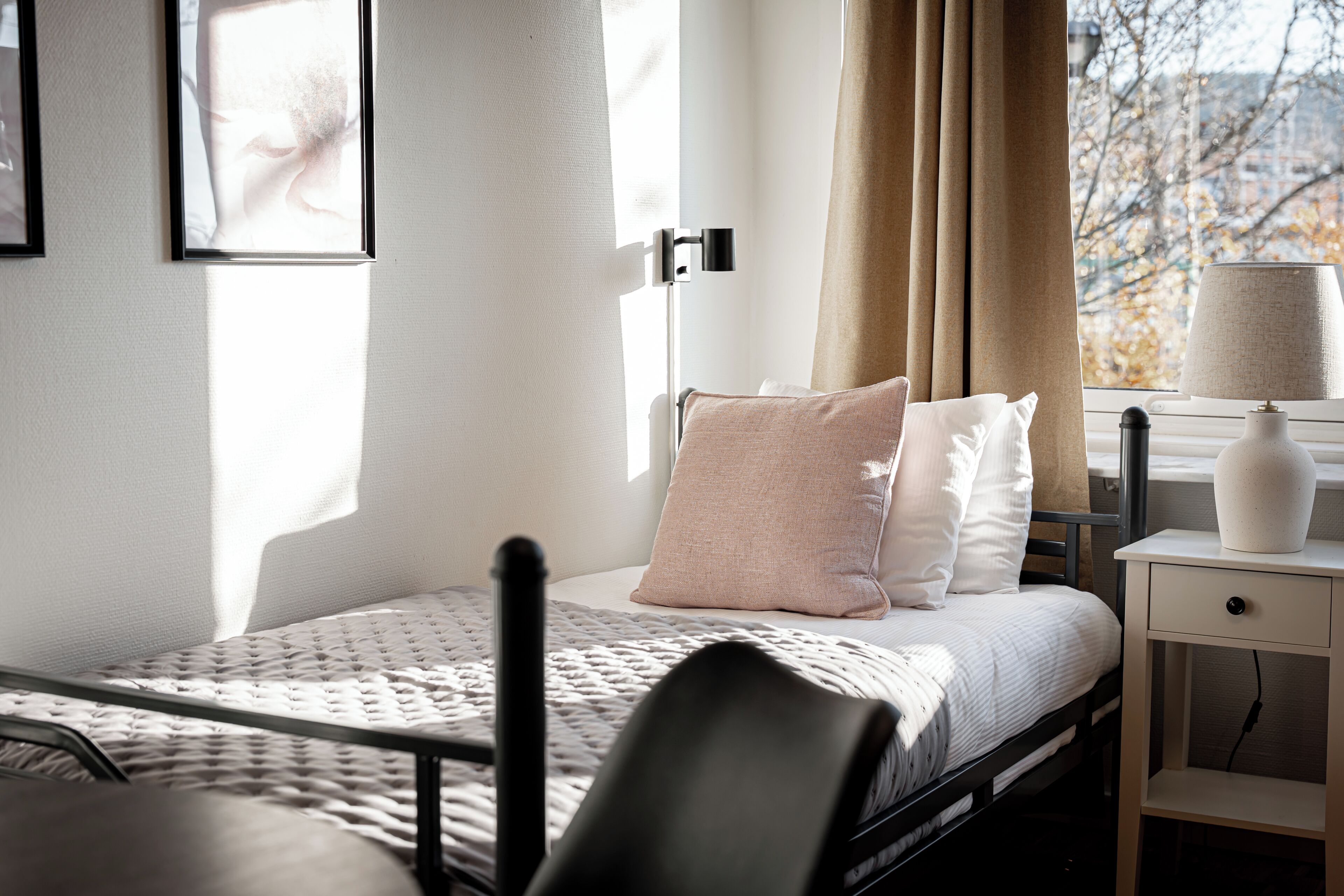 Un dormitorio ordenado con cama, mesita de noche, lámpara y una ventana con cortinas.