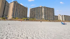 A beachfront hotel with multiple high-rise buildings, sandy beach, and a clear sky.