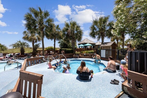 A pool area with multiple pools, palm trees, and a covered seating area.