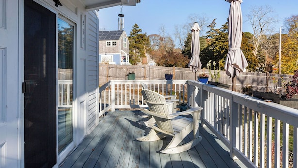 A wooden deck with a rocking chair and two umbrellas, a white railing, and a house in the background. - Wellfleet 2BR Retreat – Walk to Bay & Kayak! RPMC007 (Wellfleet)