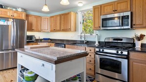 A modern kitchen with wooden cabinets, stainless steel appliances, and a granite countertop. - Wellfleet 2BR Retreat – Walk to Bay & Kayak! RPMC007 (Wellfleet)