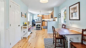 A spacious kitchen with wooden cabinets, a central island, and a dining area with a wooden table and chairs. - Wellfleet 2BR Retreat – Walk to Bay & Kayak! RPMC007 (Wellfleet)