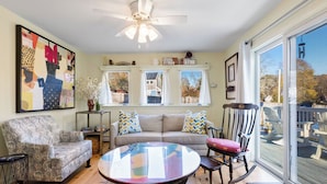 A cozy living room with a round glass coffee table, a patterned armchair, a sofa with colorful pillows, and a rocking chair. - Wellfleet 2BR Retreat – Walk to Bay & Kayak! RPMC007 (Wellfleet)