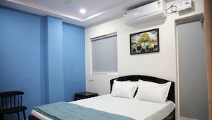A bedroom with a bed, a chair, a small table, an air conditioning unit, and a window with blinds. - PSV Grand (Hyderabad)