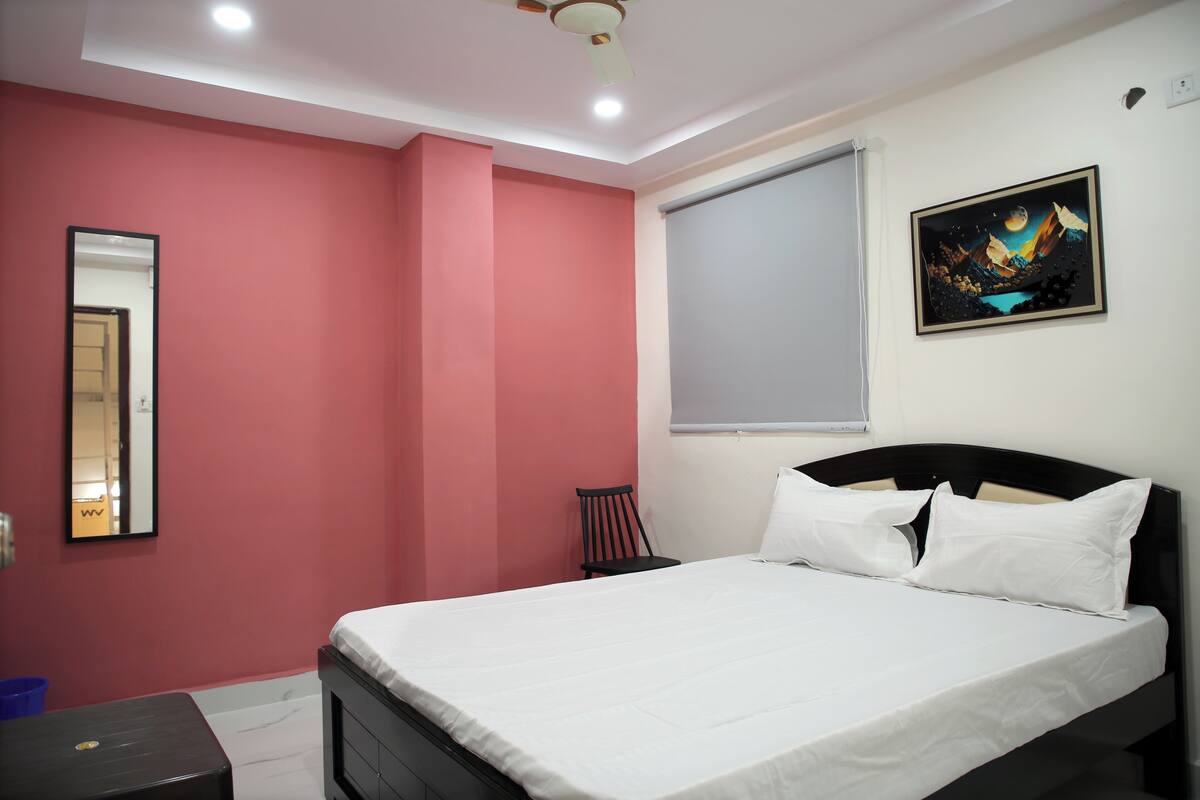 A bedroom with a bed, a chair, a window, and a painting on the wall.