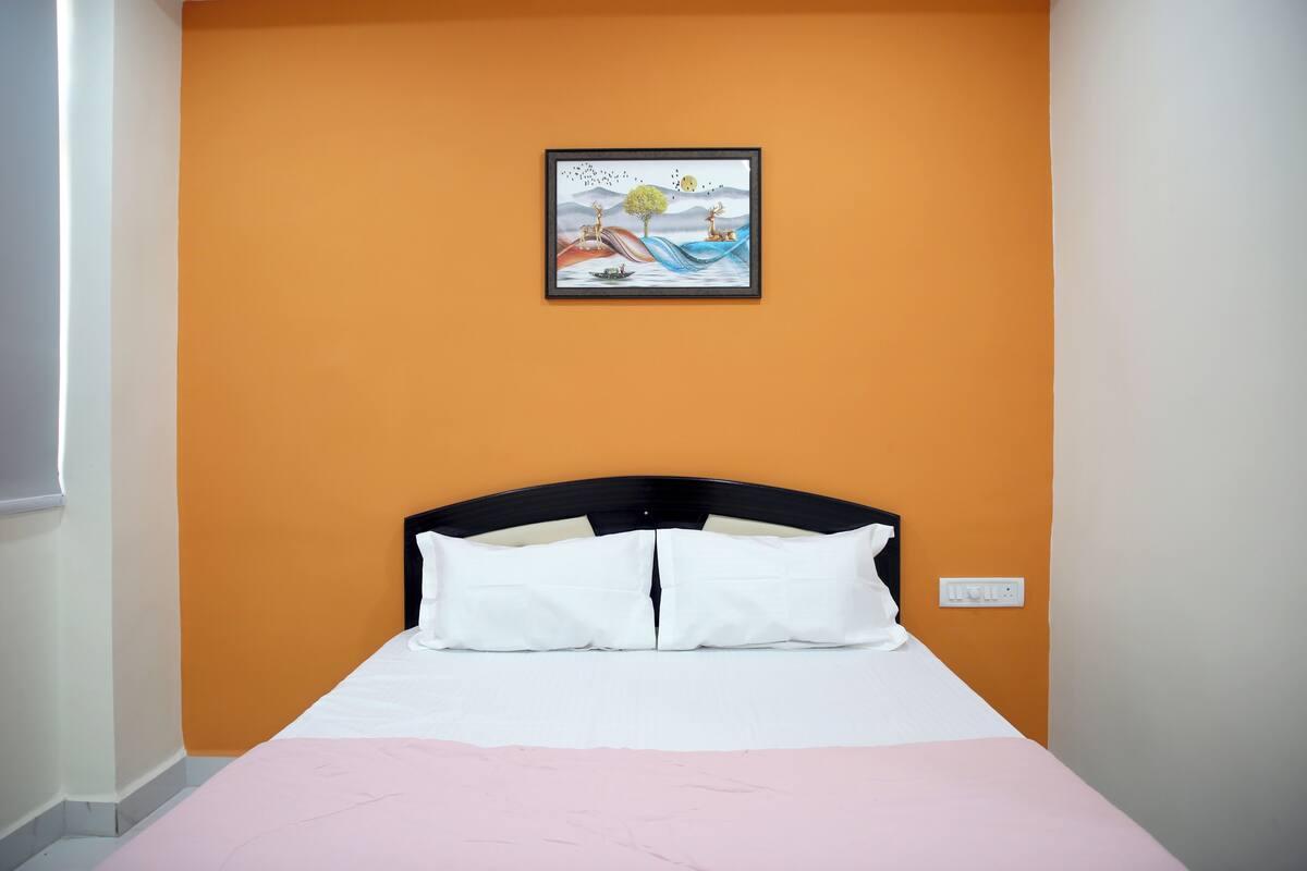 A bedroom with a bed, white pillows, a pink bedspread, and a framed picture on the wall.