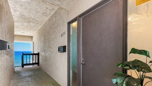 A hallway with a concrete ceiling, a door labeled "857C", a small television, and a view of the ocean. - Coastal Heights - Solana Beach Vacation Rental, Ocean Views, Pool, Pickleball (Solana Beach)