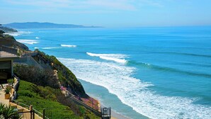 A coastal view with a building overlooking the ocean, featuring a balcony with railings and a pathway leading to the beach. - Coastal Heights - Solana Beach Vacation Rental, Ocean Views, Pool, Pickleball (Solana Beach)