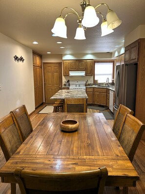 A kitchen with wooden cabinets, a stainless steel refrigerator, a wooden dining table with chairs, and a chandelier. - Hot tub, Pet friendly, directly across from GM Rec Center (Black Butte Ranch)