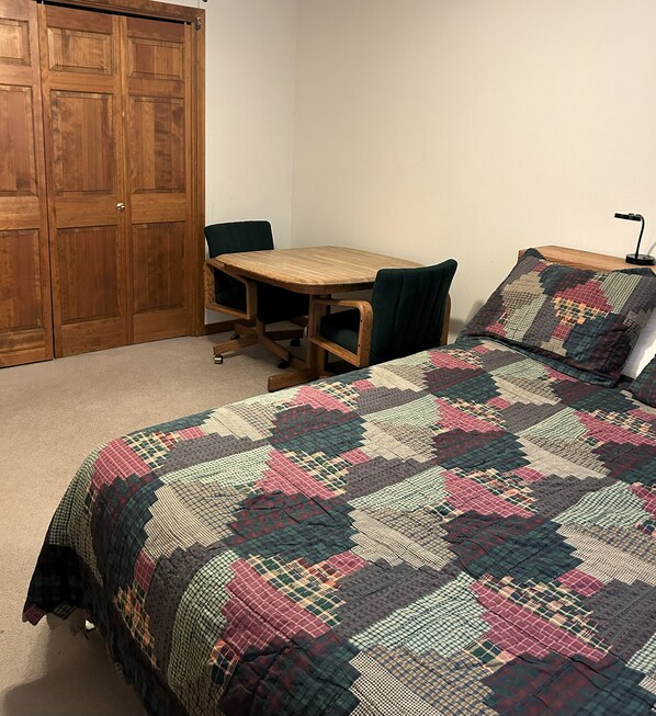 A bedroom with a wooden desk, a chair, a bed with a quilt, and a wardrobe.
