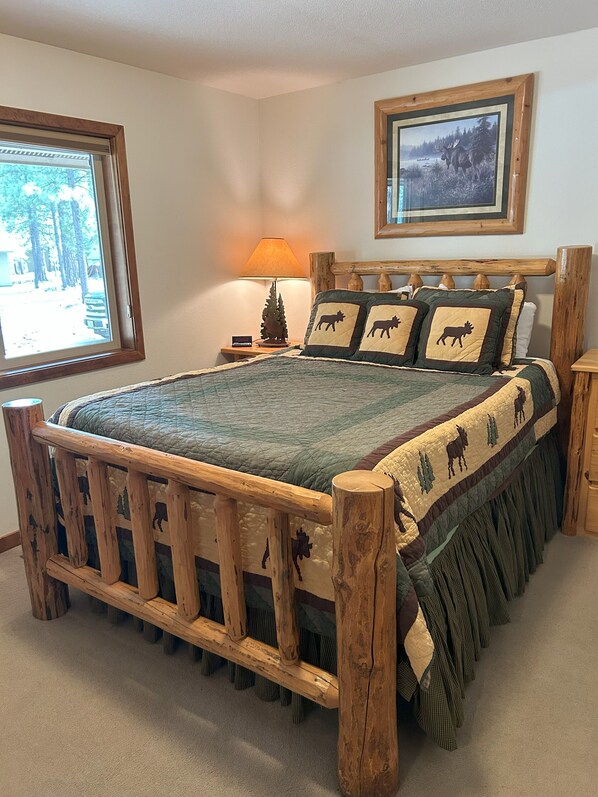 A wooden bed with a quilt featuring animal prints, a nightstand with a lamp, and a window with a view of trees. - Hot tub, Pet friendly, directly across from GM Rec Center (Black Butte Ranch)
