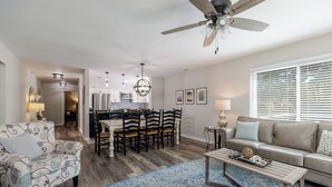 A modern living room with a sofa, a coffee table, and a dining area with chairs and a chandelier. - 25 Springwood: First Floor, 1 Level, Walk to Beach (Hilton Head Island)