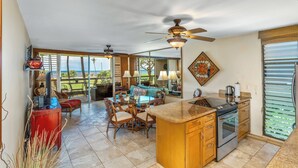 A spacious kitchen with a large island, a dining area with a view, and a ceiling fan. - Leinaala Oceanfront #205 Oceanfront Views! A/C, wifi, Pool, Great Rates! (Kihei)