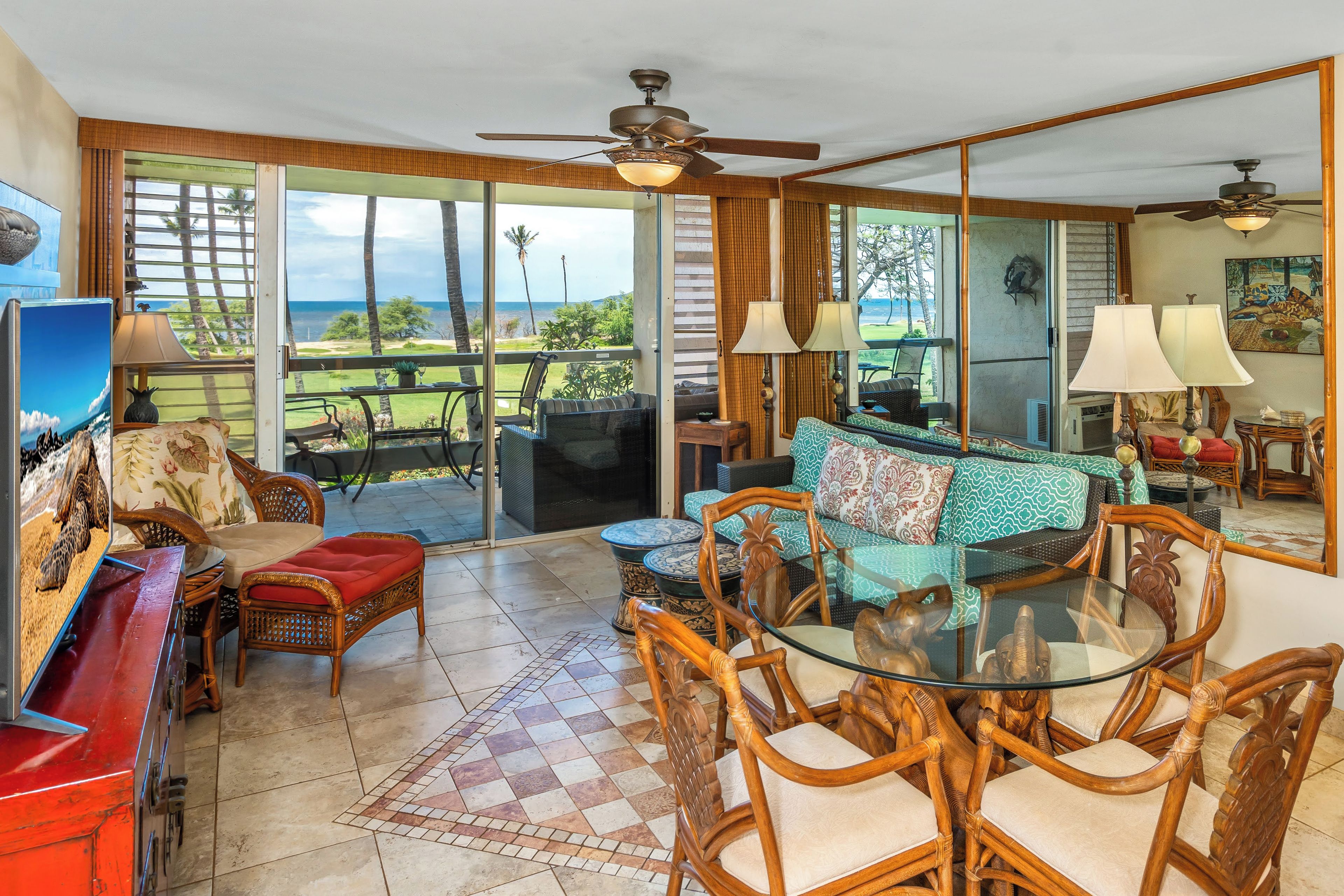 A spacious living area with a glass table and chairs, a sofa with patterned cushions, and a view of the ocean through large sliding doors.