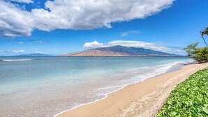 A beach with clear waters, a sandy shore, and a mountain in the background. - Leinaala Oceanfront #205 Oceanfront Views! A/C, wifi, Pool, Great Rates! (Kihei)