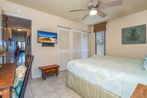 A bedroom with a bed, a ceiling fan, a painting, and a view of the hallway.