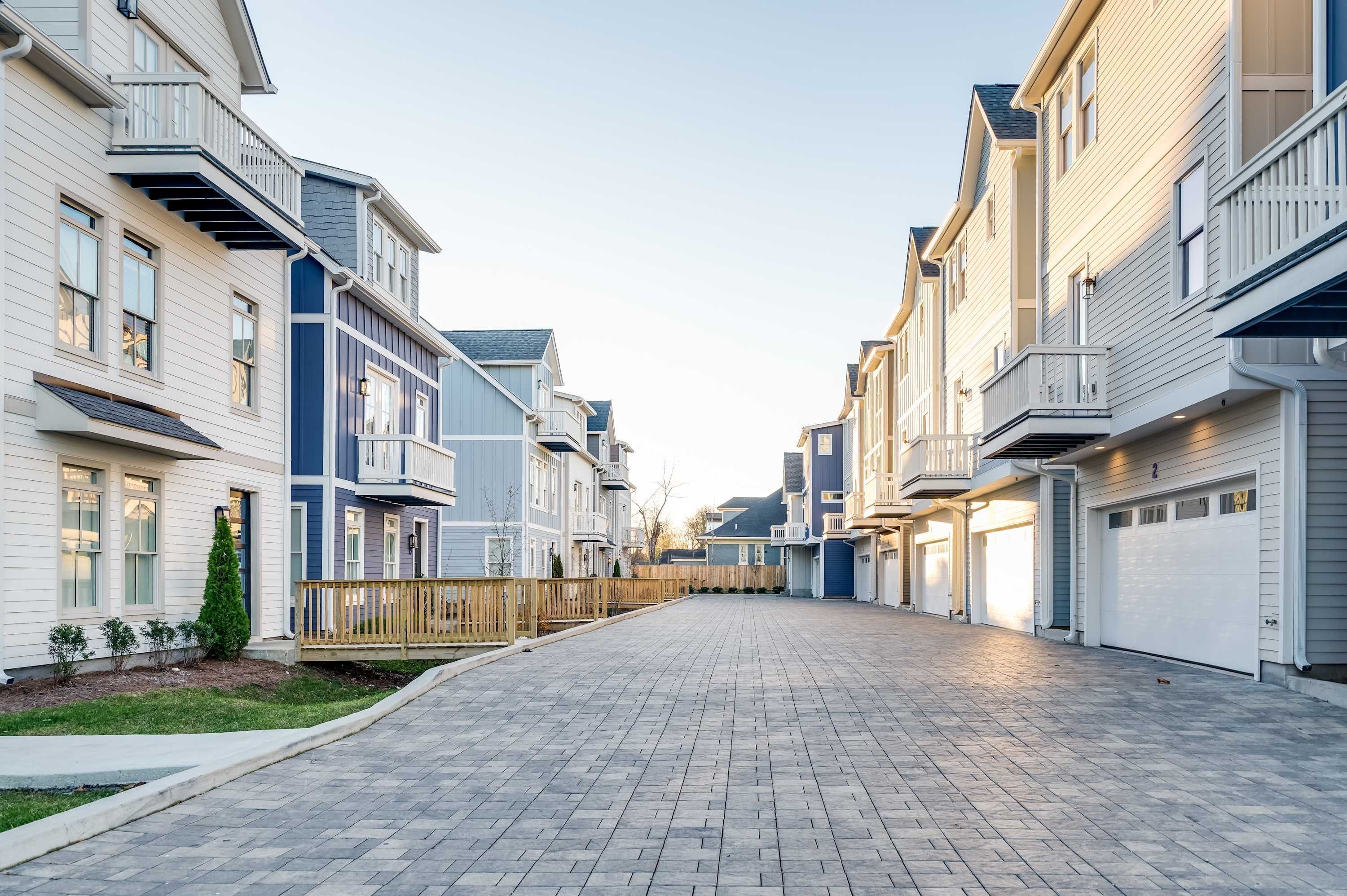 A residential street with modern houses, paved sidewalks, and a clear sky.
