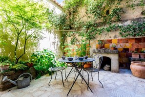 Relax in this serene patio area, surrounded by lush greenery and climbing plants, with a round table and metal chairs.