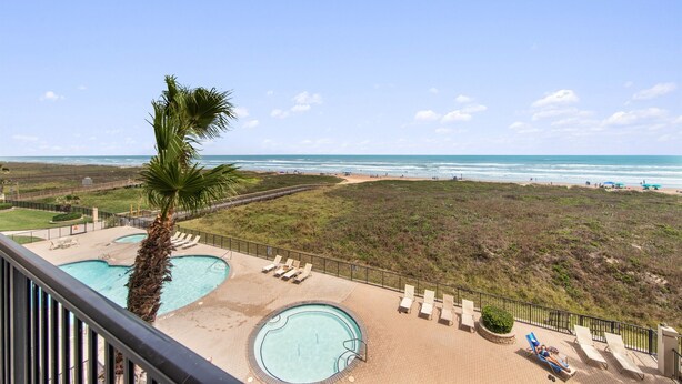 Un área de piscina con dos piscinas, una palmera y vista a la playa.