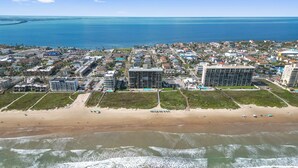 Vista aérea de un pueblo costero con una playa arenosa, propiedades frente al mar y una vista despejada del océano.