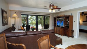 Ein Wohnzimmer mit braunem Ledersofa, Holzstühlen, einem Fernseher und einem Deckenventilator.