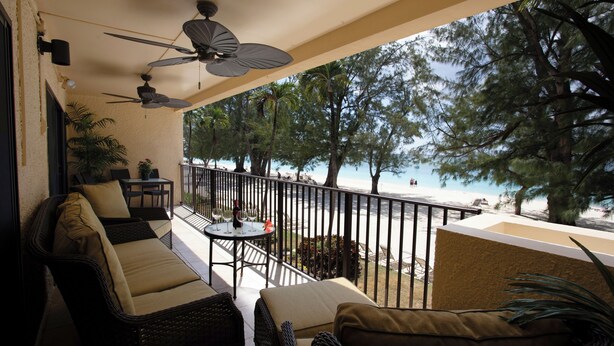 Ein Balkon mit Korbmöbeln, Deckenventilatoren und Blick auf Strand und Bäume.