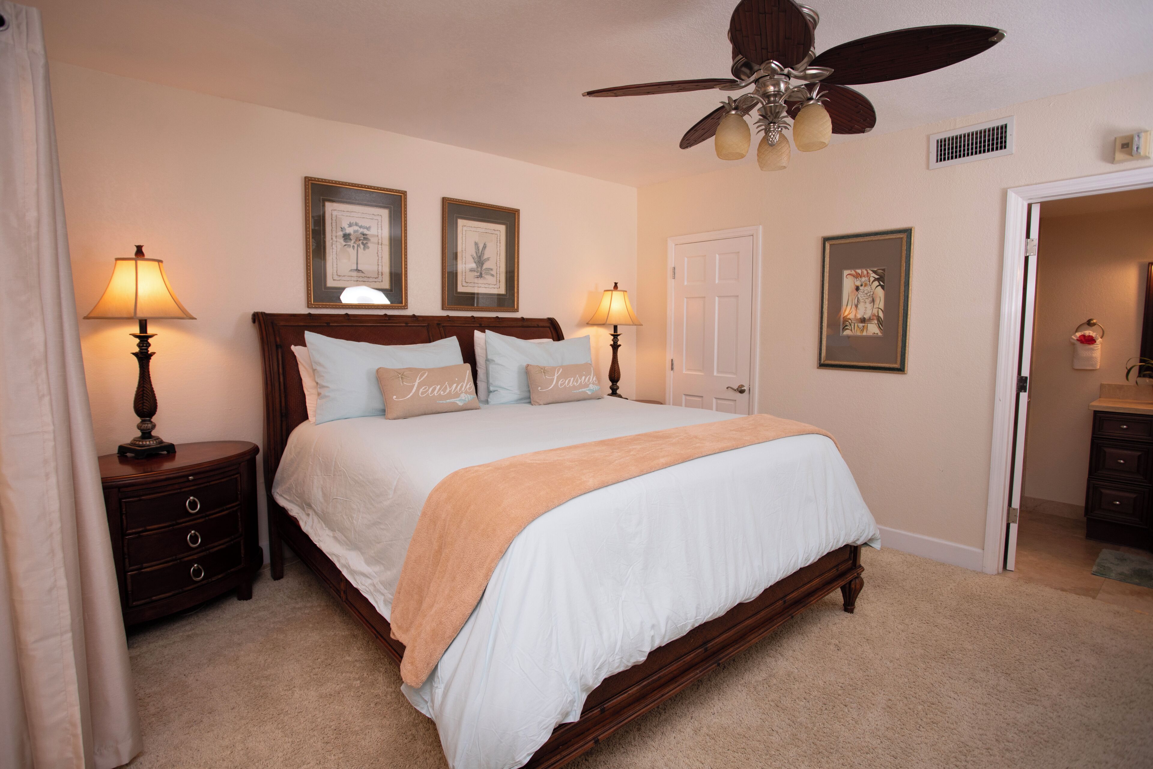 A bedroom with a bed, two bedside tables, a ceiling fan, and framed artwork on the walls.
