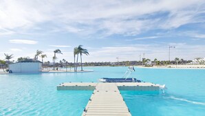 A clear blue pool with a wooden dock leading to a boat, surrounded by palm trees and a beach in the background. - Exclusive Penthouse in Santa Rosalia Lake & Life Resort El Caribe on the Costa Calida (Torre-Pacheco)