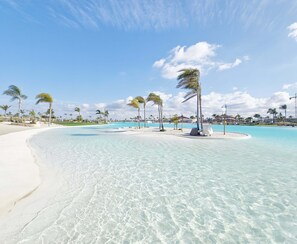 A beach resort with clear turquoise waters, white sand, and palm trees.