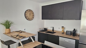 A modern kitchen with a wooden table, black cabinets, a built-in dishwasher, and a wall clock. - Luxury apartment 25m from the island's most beautiful beach, Boucan Canot. (Saint-Paul)