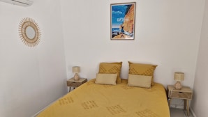 A bedroom with a bed, two nightstands, a wall-mounted mirror, and a framed picture. - Luxury apartment 25m from the island's most beautiful beach, Boucan Canot. (Saint-Paul)