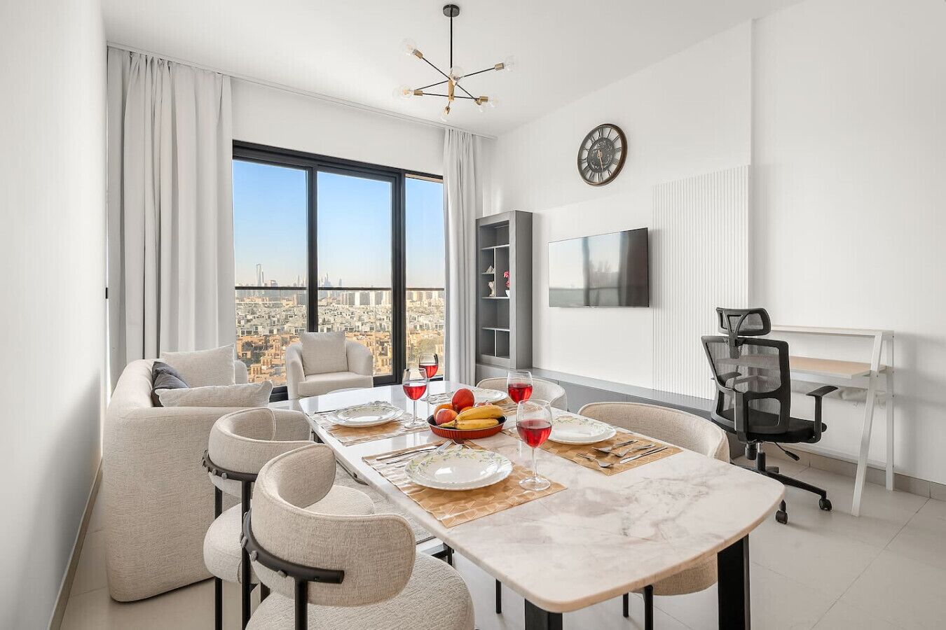 Une salle à manger moderne avec une grande table dressée pour quatre personnes, un canapé, un téléviseur et une vue sur la ville.