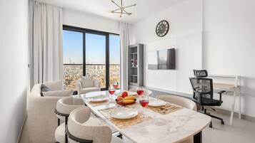 Une salle à manger moderne avec une grande table dressée pour quatre personnes, un canapé, un téléviseur et une vue sur la ville.