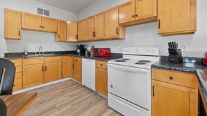 A kitchen with wooden cabinets, a white stove, and a red microwave. - Fireside Haven | Hot Tub + Downtown Walkable (Custer)