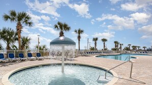 A pool area with a water fountain, lounge chairs, palm trees, and a clear sky. - Baywatch Resort #1705 3 Bedroom Condo (North Myrtle Beach)
