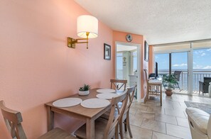 Ein Essbereich mit Tisch und Stühlen, einer Wandlampe und Blick auf das Meer durch eine Glastür.