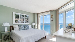 A bedroom with a large bed, a nightstand, a desk, and a view of the ocean. - Baywatch Resort #1705 3 Bedroom Condo (North Myrtle Beach)