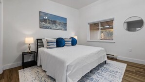 Une chambre à coucher avec un lit, une table de chevet, une lampe, un tableau, une fenêtre et un miroir.