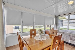 A dining area with a wooden table, chairs, a vase with flowers, and large windows with blinds. - Cozy And Relaxing Fishing Retreat 3 Bedroom Home (Okeechobee)