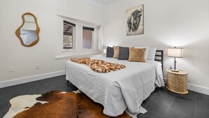 Un dormitorio con una cama, un tapete de cuero de vaca, una lámpara y un cuadro en la pared.